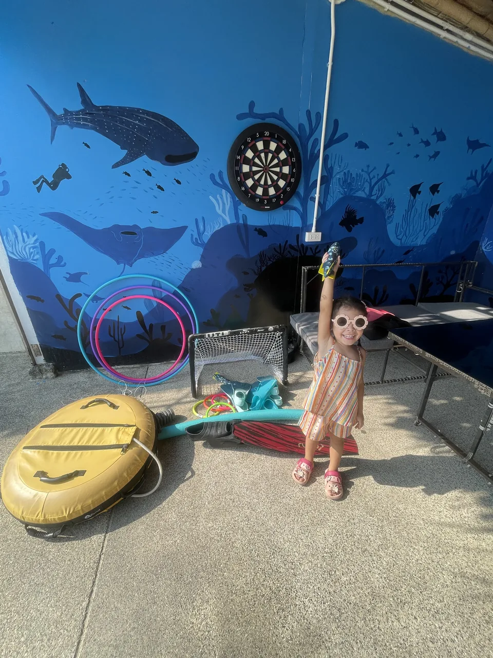 A child smiling beside freediving fins, hoops, and other pool equipment