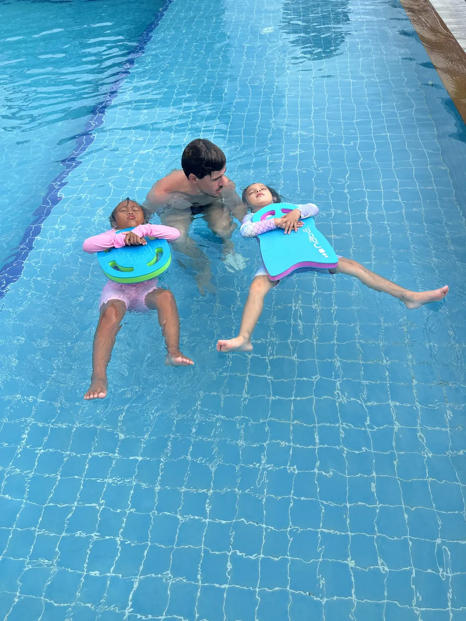 An instructor supporting two children practising floating with kickboards
