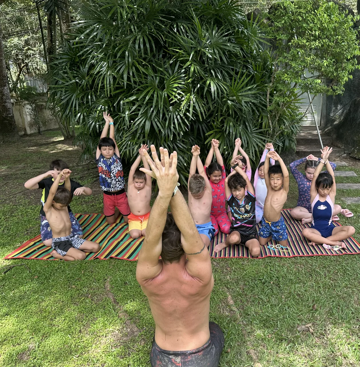 Children following an instructor in a stretching session on mats outdoors
