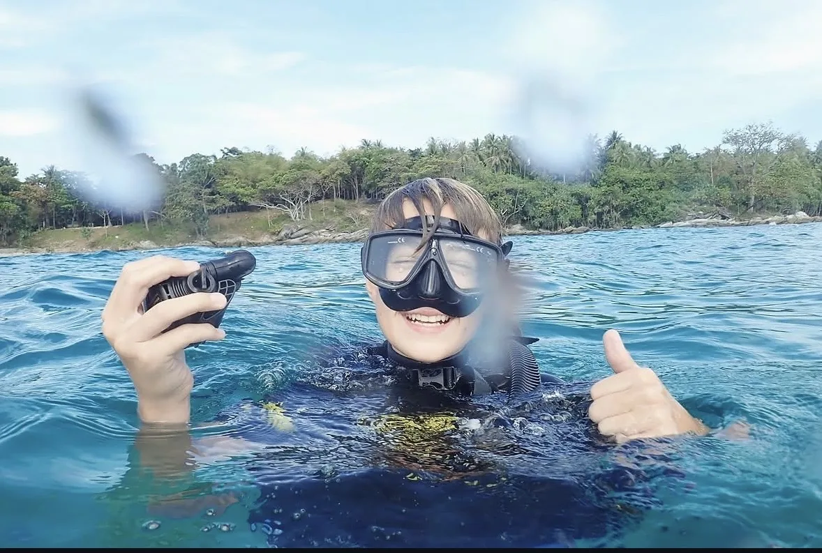 A young scuba diver smiling at the sea surface and giving a thumbs-up
