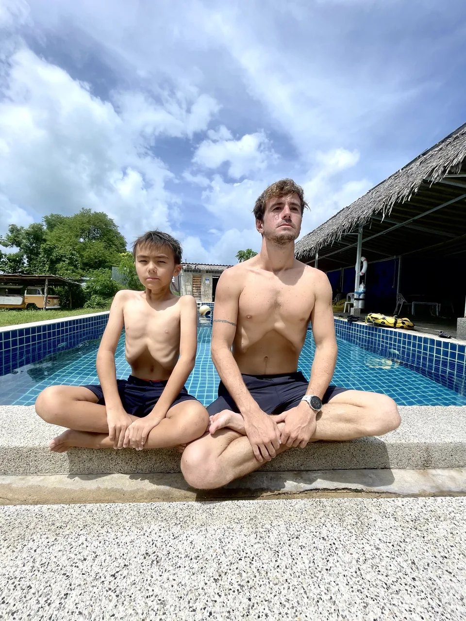 A child and instructor sitting cross-legged beside the pool