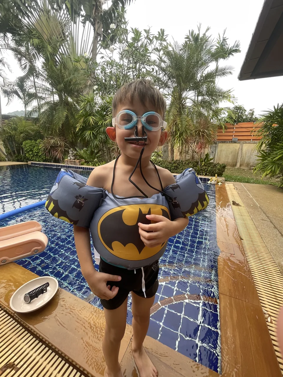 A young swimmer wearing goggles and a buoyancy aid beside the pool